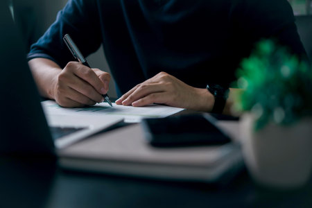 Close-up of hand writing on business report at desk. Ideal for planning, data analysis, finance,...