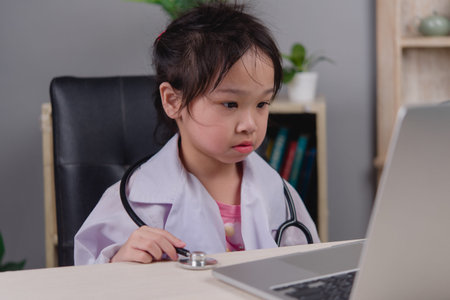 Little girl dressed as a doctor using a laptop, representing role play, future healthcare career,...