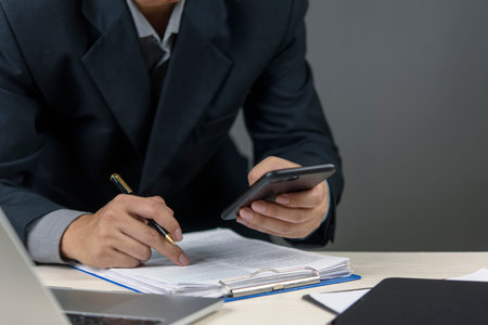 Close-up of hands managing paperwork and a mobile phone, representing financial transactions, legal...