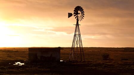 Windmill at sunrise on a farm with a water damの写真素材