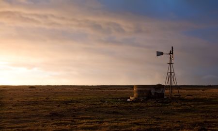 Windmill at sunrise on a farm with a water damの写真素材