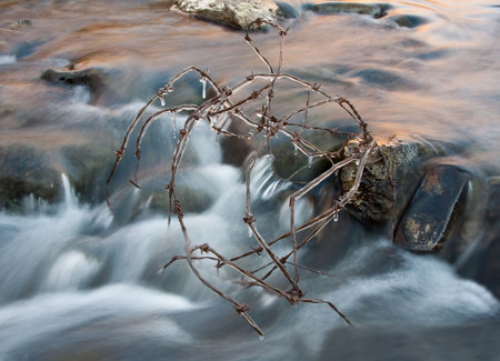 Icicles on barbed wire in cold stream with flowing waterの写真素材