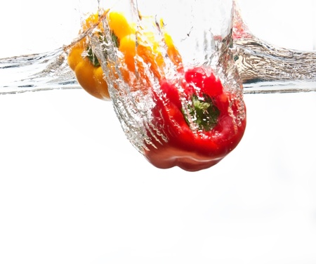 Yellow and red pepper falling into cristal clear waterの写真素材