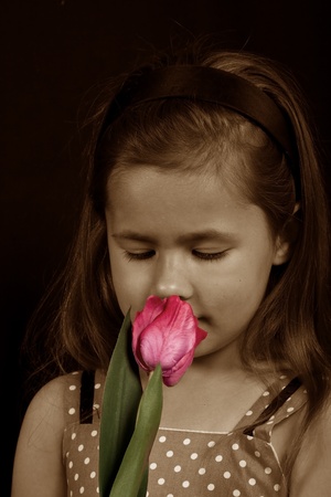 A small girl smelling a pink flower in sepia color toneの写真素材