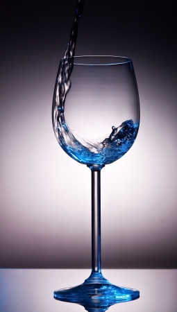 Liquid poured into backlid wine glass with blue impressionの写真素材