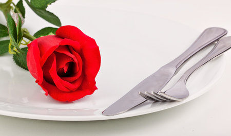 Dinner plate with red rose and silver cutlery before a romantic dinner