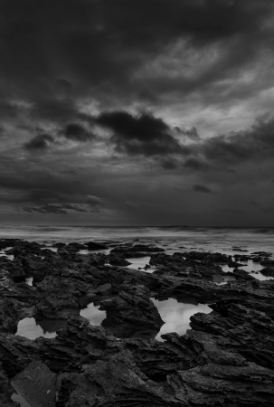 Sunrise landscape of ocean with waves clouds and rocks black and whiteの写真素材