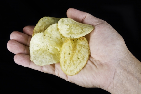 Hand holding potato chips on black backgroundの写真素材