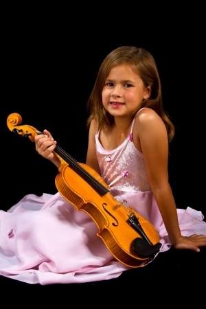 Girl holding violin in pink dress concentration on blackの写真素材