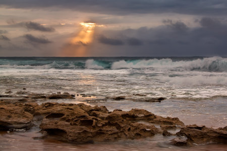 Sunrise landscape of ocean with waves clouds and rocks on beach