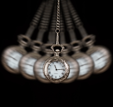 Pocket watch silver swinging on a chain black background to hypnotiseの写真素材