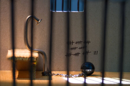 Conceptual jail photo with iron nail ball and chain behind out of focus bars and windowの写真素材
