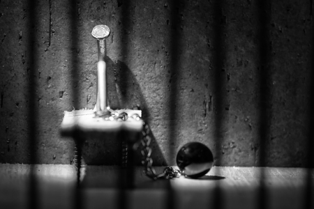 Conceptual jail photo with iron nail ball and chain behind out of focus bars artistic conversionの写真素材