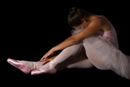 Female dancer sit on floor looking sad in pink tutu and slippers low keyの写真素材