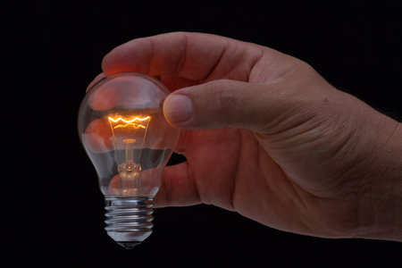 Human hand holding a light bulb to conserve energy in darkness