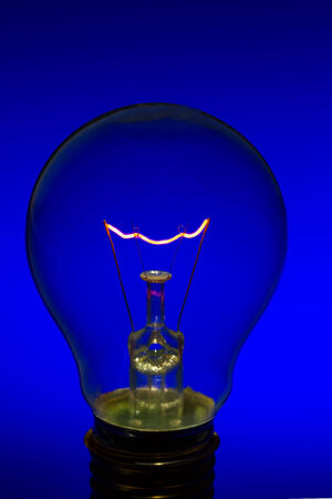 Glass light bulb with burning filament upright with bright blue backgroundの写真素材