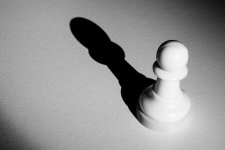 Chess pawn standing in a spotlight that make a shadow with darknessの写真素材