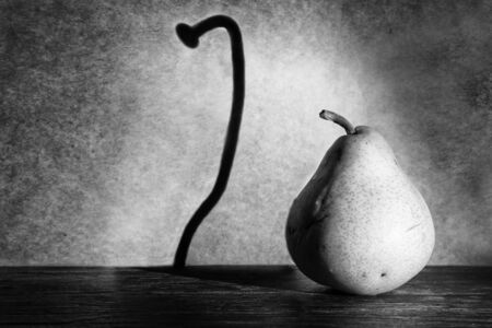 Fat pear makes a thin nail shadow on wall in spotlight gunge artistic conversionの写真素材