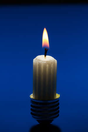 Light bulb fitting with no glass and short candle standing on bright blue surfaceの写真素材