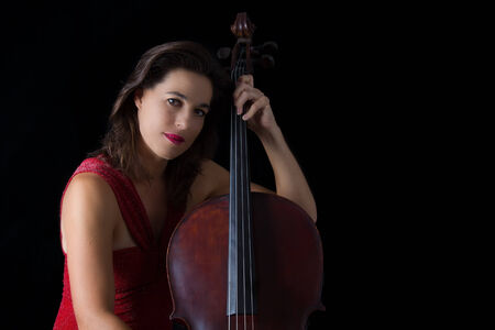 Beautiful brunette playing a cello with selective light in red dressの写真素材