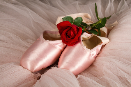 Old used ballet slippers lying on floor with rose and pink tutuの写真素材