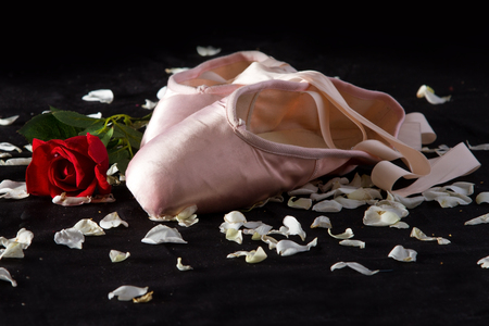 Old used ballet slippers lying on floor with rose and petalsの写真素材