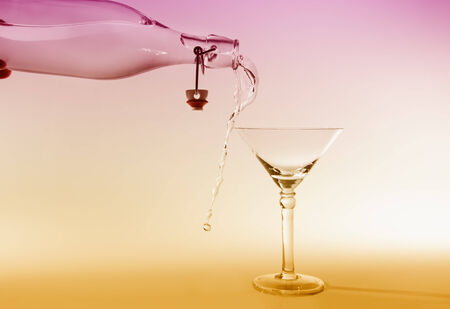 Clear water pour out of bottle splash into glass and spill with a pink and yellow back lightingの写真素材