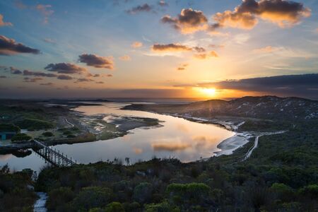 Cloudy sunrise over a quiet lagoon with cloud patterns reflected in the waterの写真素材