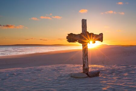 An old cross on a sand dune next to the ocean with a calm sunriseの写真素材