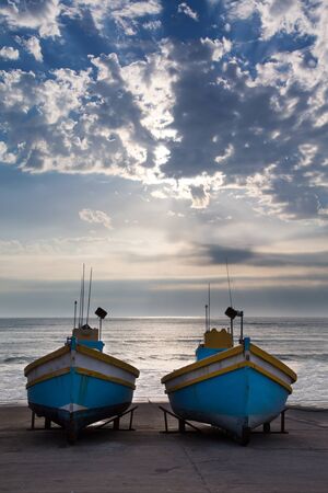 Row of old fishing boats in a small harbour next to the ocean in the morningの写真素材