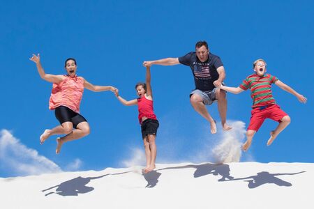Happy family of four jump from a high white sand dune having funの写真素材