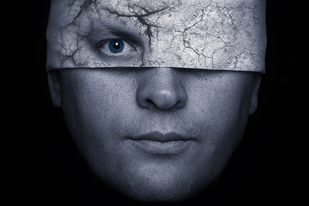 Face of man with a cracked blindfold and eye looking throughの写真素材