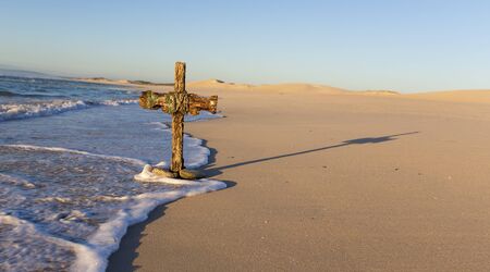 An old cross on a sand dune next to the ocean with a calm sunriseの写真素材