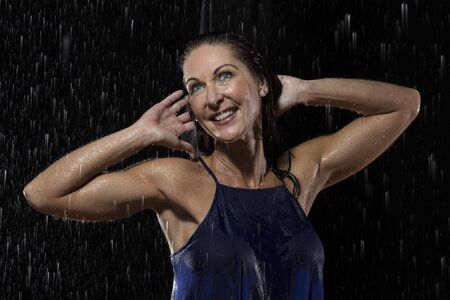 Beautiful woman in blue dress stands in rain at night getting wetの写真素材