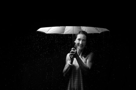 Beautiful woman with pink dress standing in rain under an umbrella at night