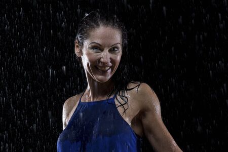 Beautiful woman in blue dress stands in rain at night getting wetの写真素材