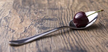 Close-up of cherries in a silver spoon on brown wood backgroundの写真素材