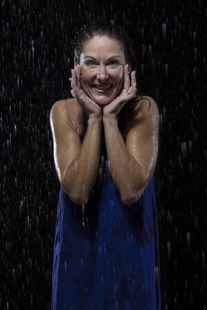 Beautiful woman in blue dress stands in rain at night getting wetの写真素材