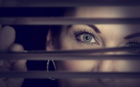 Portrait of a woman standing in the dark looking through blinds artistic conversionの写真素材