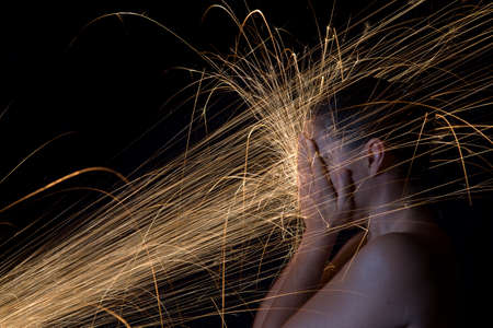 Long exposure photo of a woman blocking glowing sparks artistic conversionの写真素材