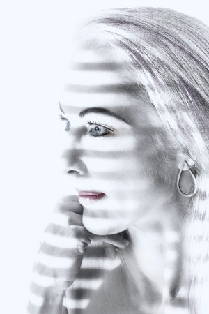 Portrait of a woman standing in light looking through blinds artistic conversionの写真素材