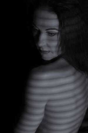 Portrait of a woman posing in the dark with shadow lines of blinds artistic conversionの写真素材