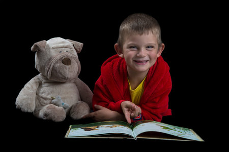 Funny boy with a stuffed dog reading a book before bed timeの写真素材