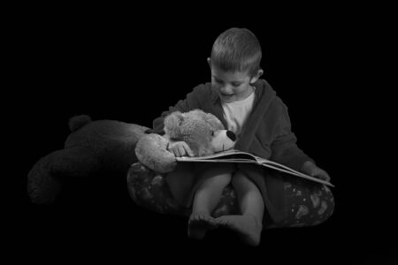 Funny boy with a teddy bear reading a book before bed time in artistic conversionの写真素材