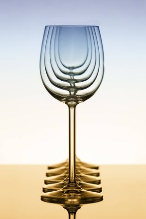 Row of empty wine glasses standing on a reflective surface with a perfect reflection with blue and range tintの写真素材