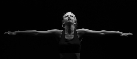 Beautiful fit and healthy blond woman in black top in the dark with arms stretched artistic conversionの写真素材