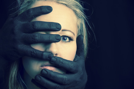 Frightened blonde woman grabbed by black hands on her face in artistic conversionの写真素材