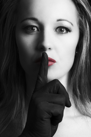 Frightened blonde woman silenced with finger in black on her face with red lips in artistic conversionの写真素材