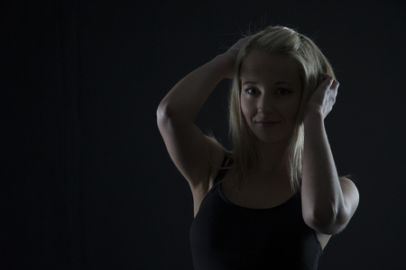 Beautiful blond woman in black top in the dark with selective lighting and hands in hairの写真素材