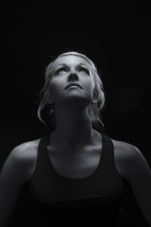 Beautiful fit and healthy blond woman portrait in black top in the dark with selective lighting artistic conversionの写真素材